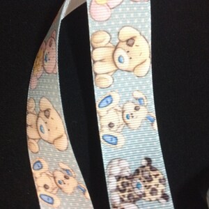 May include: Blue ribbon with a white background and a repeating pattern of cartoon dogs. The dogs are brown, white, and black with blue accents. The ribbon has a white polka dot pattern.