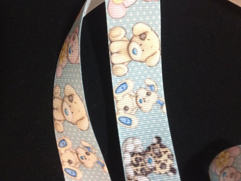 May include: Blue ribbon with a white background and a repeating pattern of cartoon dogs. The dogs are brown, white, and black with blue accents. The ribbon has a white polka dot pattern.