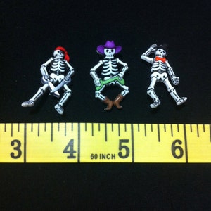 May include: Three skeleton figurines, each wearing a different hat. The skeleton on the left is wearing a red pirate hat and holding a sword. The skeleton in the middle is wearing a purple cowboy hat and holding a green lasso. The skeleton on the right is wearing a black top hat and a red bow tie. The skeletons are approximately 1 inch tall.