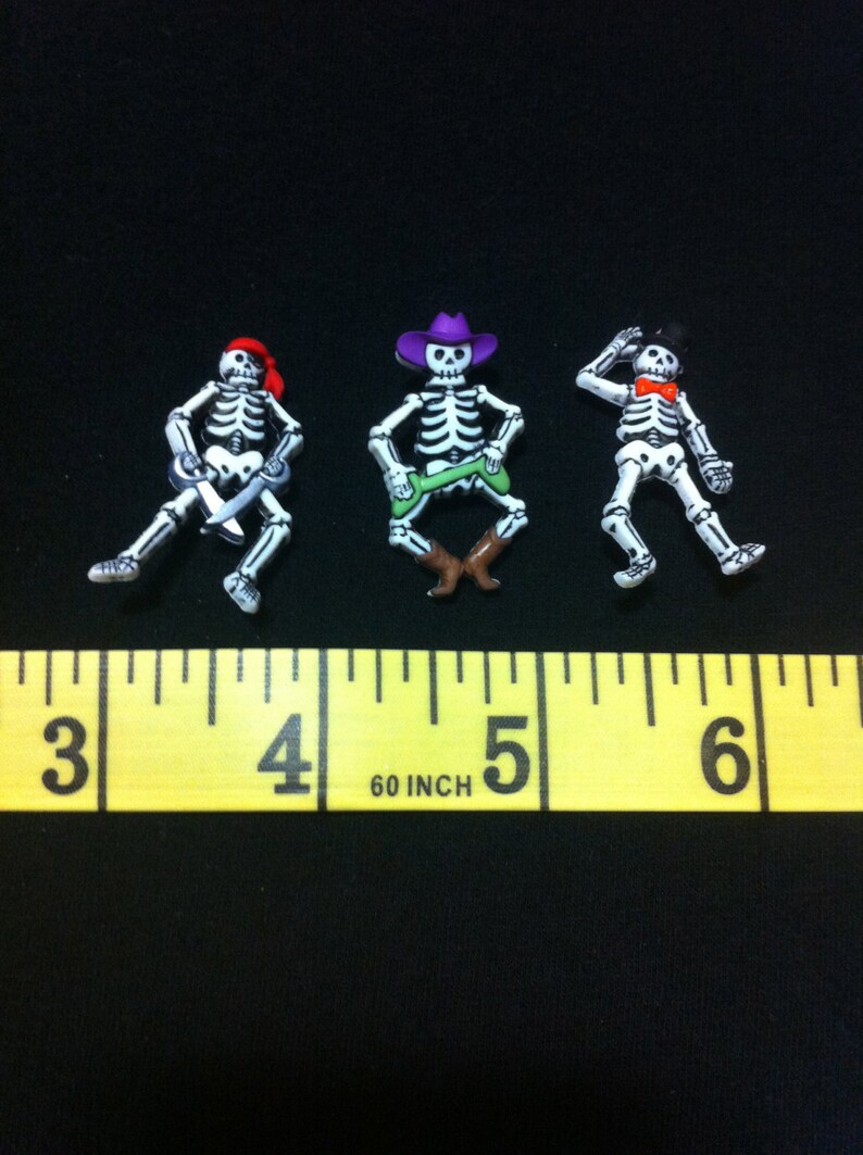May include: Three skeleton figurines, each wearing a different hat. The skeleton on the left is wearing a red pirate hat and holding a sword. The skeleton in the middle is wearing a purple cowboy hat and holding a green lasso. The skeleton on the right is wearing a black top hat and a red bow tie. The skeletons are approximately 1 inch tall.