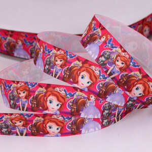 May include: Pink satin ribbon with a repeating pattern of a cartoon princess with a crown, a squirrel, and birds. The princess is wearing a purple dress and has long red hair.