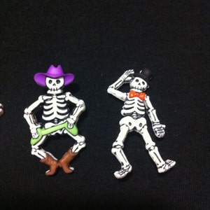 May include: Two skeleton figurines, one wearing a purple cowboy hat and green pants, the other wearing a black top hat and a red bow tie.