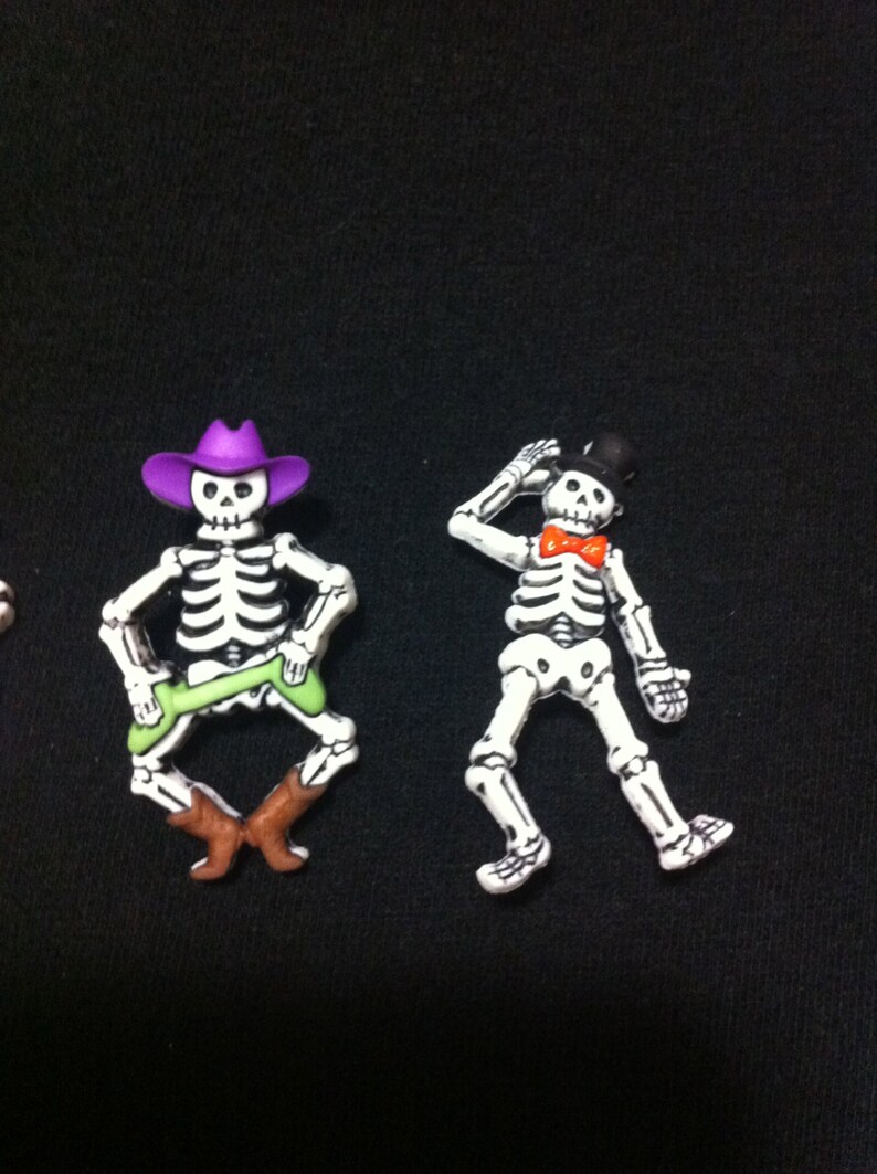 May include: Two skeleton figurines, one wearing a purple cowboy hat and green pants, the other wearing a black top hat and a red bow tie.