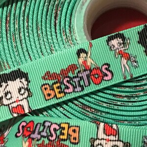 May include: A roll of green ribbon with a repeating pattern of a cartoon character and the word "Besitos".