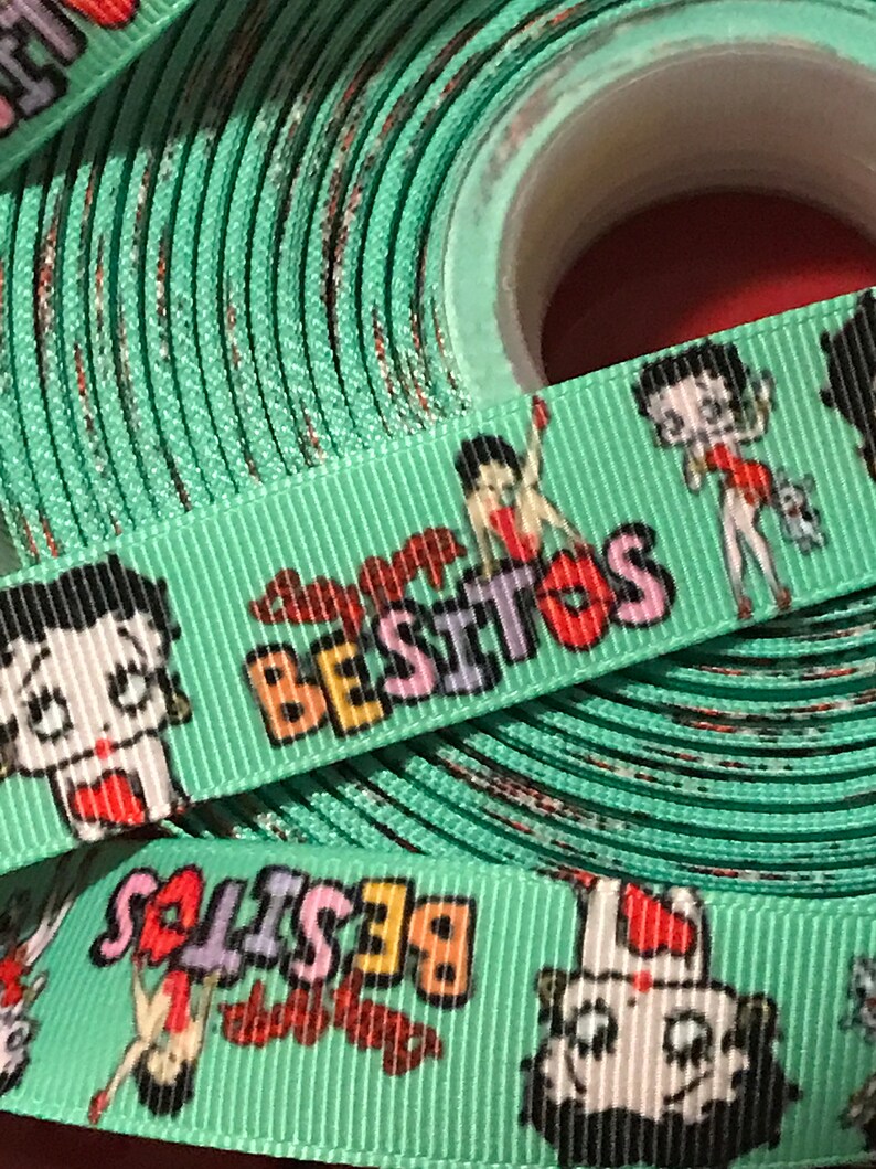 May include: A roll of green ribbon with a repeating pattern of a cartoon character and the word "Besitos".