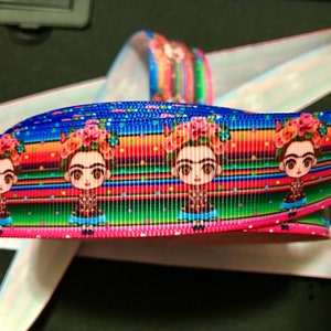 May include: A colorful ribbon with a repeating pattern of Frida Kahlo's portrait, flowers, and a striped background. The ribbon is blue, green, red, orange, and pink.