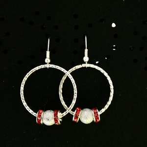 May include: Silver hoop earrings with a textured finish and a red rhinestone bead accent.