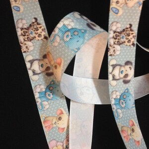 May include: Blue and white ribbon with a repeating pattern of cartoon teddy bears. The ribbon is made of a soft, textured fabric.