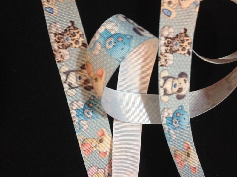 May include: Blue and white ribbon with a repeating pattern of cartoon teddy bears. The ribbon is made of a soft, textured fabric.