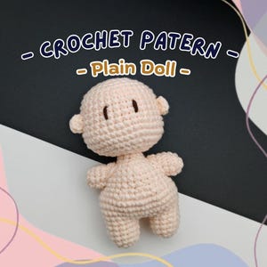 May include: A crocheted plain doll in a light peach color. The doll has a rounded head with small ears, simple facial features, and a small body with arms and legs. The text "CROCHET PATTERN - Plain Doll -" is displayed above the doll.