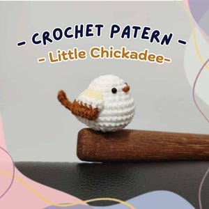 May include: A handmade crochet bird, a "Little Chickadee", perched on a wooden stick. The bird is white with brown wings and tail, and black eyes. The text "CROCHET PATTERN - Little Chickadee-" is displayed above the bird.