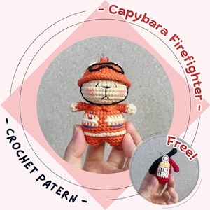 Könnte beinhalten: Ein gehäkeltes Capybara-Feuerwehrmann mit orangefarbener Uniform und Hut mit schwarzer Brille. Die handgefertigte Amigurumi-Figur hat einen Schlüsselanhänger. Das Bild enthält auch einen kleinen gehäkelten Feuerlöscher.