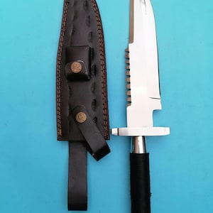 May include: A stainless steel hunting knife with a serrated spine and a black wrapped handle, next to a brown leather sheath with decorative stitching and a snap closure. The knife has a silver bolster and a textured end cap.
