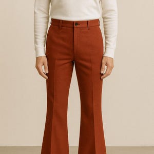 May include: Rust-colored flared trousers with a button closure and belt loops. The pants are paired with a white long-sleeve shirt and black leather shoes. The trousers have a classic, tailored fit.