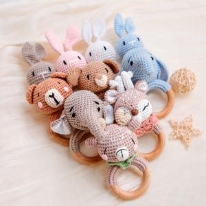 May include: A collection of handmade crochet animal rattles featuring various creatures including a bear, elephant, deer, and rabbits. Each plush animal head is securely attached to a smooth, round, natural wooden ring, creating a tactile toy.
