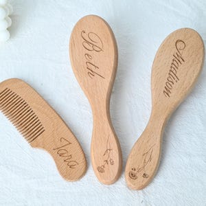 May include: A set of three wooden baby hair care items: a comb and two brushes. The comb and brushes are engraved with the names "Tara", "Beth", and "Madison". The brushes have a floral design. The items are made of light-colored wood.