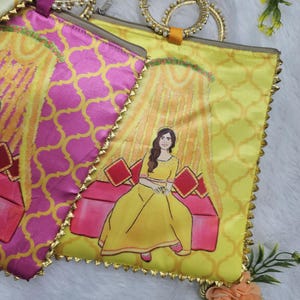 Op de afbeelding: Close-up van twee decoratieve stoffen tassen. Eén tas is geel met een vrouw in een gele jurk, de andere is roze met een herhalend patroon. Beide tassen hebben gouden randen en handvatten.