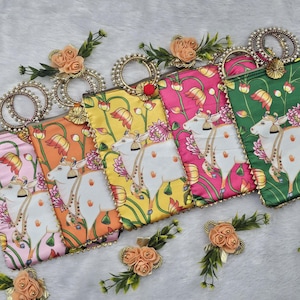 May include: A collection of colorful, patterned clutch bags. Each bag features a white cow illustration with floral accents and a decorative handle. The bags are in shades of pink, orange, yellow, and green, with floral embellishments.