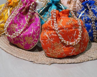May include: A collection of colorful, embroidered drawstring bags in various shades, including pink, orange, and blue. Each bag is adorned with gold thread and a beaded handle, resting on a woven mat. The bags are likely for carrying small items.