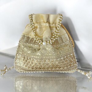 Könnte beinhalten: Cremefarbener Beutel mit Kordelzug, aufwendiger Goldstickerei und Pailletten. Die Tasche hat einen Perlenhenkel und Quastenakzente. Ein Perlschmuck verleiht diesem Accessoire einen Hauch von Eleganz.