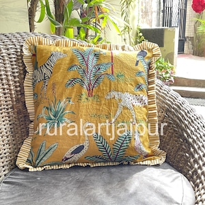 Könnte beinhalten: Senfgelbes Zierkissen mit einem Safari-Tierdruck mit Zebras, Leoparden und Vögeln. Das Kissen hat einen gerüschten Rand mit einem Streifenmuster und dem Text "ruralartjaipur". Das Kissen liegt auf einem Korbstuhl.