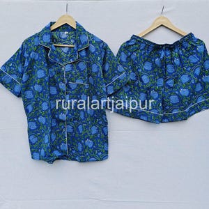 May include: Blue floral print pajama set. The set includes a short-sleeved button-down shirt and matching shorts. Both pieces have a white trim and are hanging on wooden hangers. The text "ruralartjaipur" is visible on the shirt and shorts.