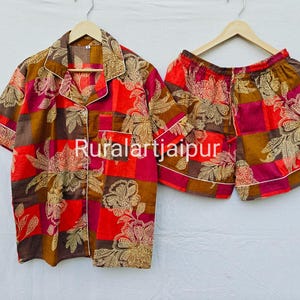 Peut inclure: Un ensemble de pyjama deux pièces à motif floral. L'ensemble comprend une chemise boutonnée à manches courtes et un short assorti. Le tissu présente un mélange de couleurs rouge, marron et or. Le texte "Ruralartjaipur" est visible sur la chemise.