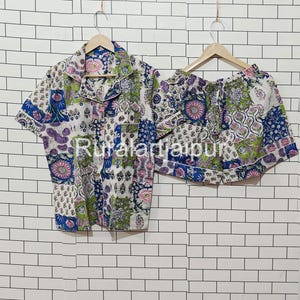 Peut inclure: Un ensemble de pyjama deux pièces avec un motif floral dans les tons de bleu, vert, rose et blanc. L'ensemble comprend une chemise boutonnée à manches courtes et un short assorti. Le texte "Rural Jaipur" est visible sur la chemise.