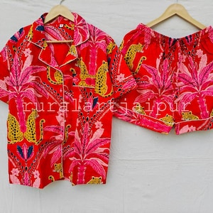 May include: A red pajama set consisting of a short-sleeved button-down shirt and matching shorts. The fabric features a vibrant print of yellow leopards, pink palm trees, and floral motifs. The text "ruralartjaipur" is visible across the center.