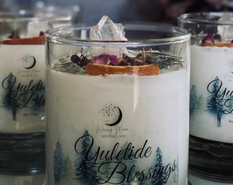 May include: A clear glass candle jar with a white candle and a crystal on top. The candle is decorated with a wintery forest scene and the text "Yuletide Blessings" and "Waxing Moon Apothecary". The jar is 9 oz / 255g.