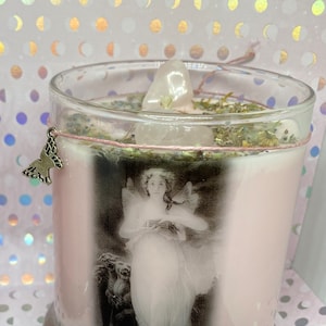 May include: A clear glass jar candle with a pink wax base and a white crystal on top. The jar has a black and white image of a woman with wings and the word "Psyche" written below the image.
