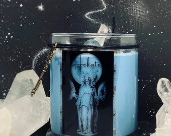 May include: A blue glass candle jar with a black label featuring a depiction of Hekate, the Greek goddess of magic, with three moons behind her. The label also includes the word "Hekate" in a stylized font.