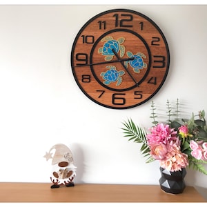 May include: A round wooden wall clock with a black frame and numbers. The clock face features a wood grain pattern and three blue sea turtle designs. A small wooden gnome figurine and a vase of flowers are also visible.
