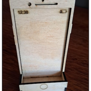 May include: A wooden phone-shaped box with a light brown interior and black trim. The time "12:38" is displayed on the screen. The box has a small rectangular opening at the bottom and a circular design on the front.