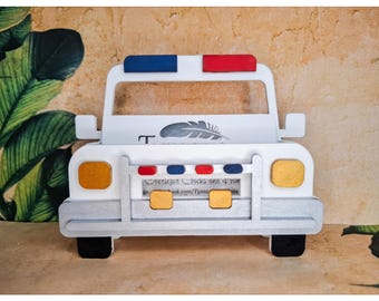Può includere: Un porta carte bianco a forma di auto con accenti blu e rossi sulla parte superiore. La parte anteriore presenta dettagli dorati e argentati, tra cui luci rettangolari e un paraurti. Un disegno di piuma grigia è visibile sulla parte anteriore. Il porta carte ha ruote nere.