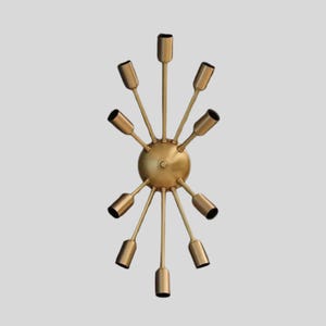 Puede incluir: Un candelabro dorado de estilo Sputnik con diez brazos que se extienden desde una esfera central. Cada brazo termina en un casquillo cilíndrico con forro negro. El accesorio está diseñado para iluminación.