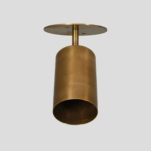 May include: A gold-colored, cylindrical pendant light fixture with a circular top. The light has a smooth, metallic finish and a modern design. The fixture is suspended from the ceiling, showcasing its minimalist aesthetic.