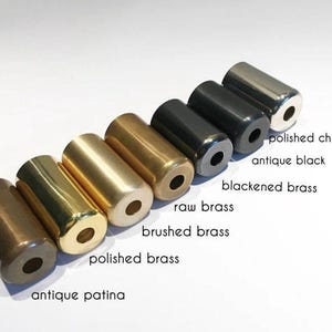 Puede incluir: Una variedad de objetos cil&iacute;ndricos de metal en varios acabados, incluyendo p&aacute;tina antigua, lat&oacute;n pulido, lat&oacute;n cepillado, lat&oacute;n crudo, lat&oacute;n ennegrecido, negro antiguo y cromo pulido. Cada uno tiene un agujero en el extremo, con etiquetas.