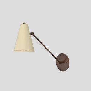 May include: A wall-mounted lamp featuring a cream-coloured conical shade and a dark brown, adjustable arm. The lamp has a circular base and a vintage aesthetic, suitable for interior lighting.
