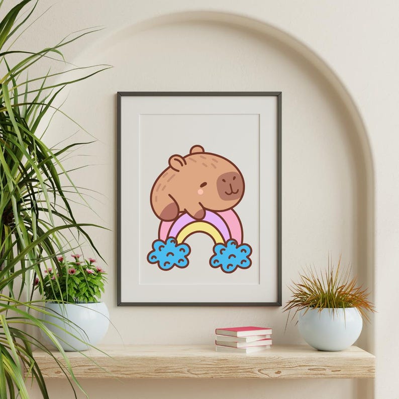 Op de afbeelding: Een ingelijste kunstdruk met een cartoon capibara op een regenboog. De capibara is bruin en de regenboog heeft roze, gele en blauwe kleuren. Het kunstwerk wordt tentoongesteld op een houten plank met planten en boeken.