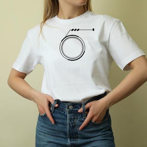 May include: White t-shirt featuring a black graphic design. The design includes a circle with a line and three short lines above it, and a dot on the right side. The shirt is made of a soft material.