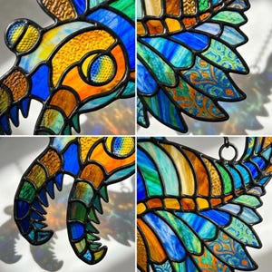 May include: A stained glass butterfly in vibrant colours. The wings display blue, green, orange, and yellow hues, with patterned details. The butterfly is outlined in black and has a metal ring for hanging. A decorative item.