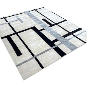 May include: A rectangular area rug with a geometric design. The rug features a cream-colored background with a pattern of black and gray lines. The lines intersect to create a modern, abstract design. The rug is made of a soft, plush material.