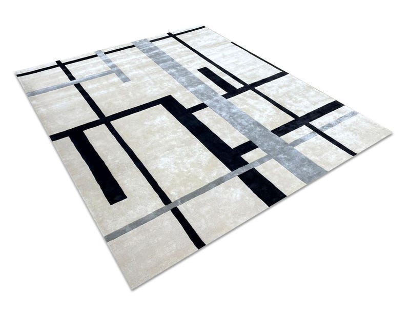 May include: A rectangular area rug with a geometric design. The rug features a cream-colored background with a pattern of black and gray lines. The lines intersect to create a modern, abstract design. The rug is made of a soft, plush material.