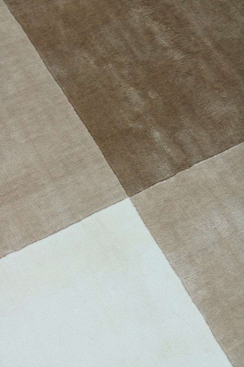 Pu&ograve; includere: Primo piano di un tappeto con un motivo geometrico. Il tappeto &egrave; diviso in quattro sezioni, ciascuna con una diversa tonalit&agrave; di colore neutro. I colori includono bianco, beige, marrone chiaro e marrone scuro. Il tappeto ha una consistenza morbida e soffice.