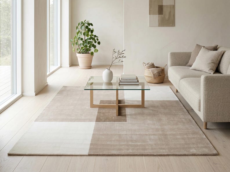 Pu&ograve; includere: Un soggiorno moderno con un tappeto beige con blocchi di colore geometrici, un tavolino con piano in vetro e un divano dai toni neutri. Una pianta in vaso e oggetti decorativi completano l'estetica minimalista.