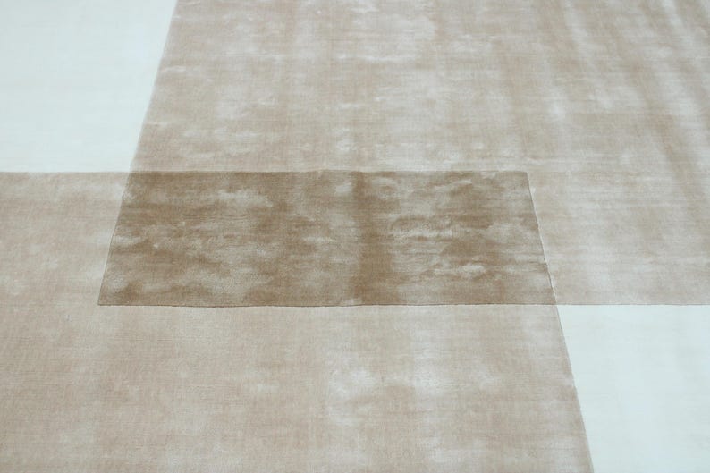 Pu&ograve; includere: Un tappeto moderno con un design geometrico. Il tappeto presenta una combinazione di sezioni beige e bianco sporco, creando un effetto a strati. La sezione centrale &egrave; di una tonalit&agrave; beige pi&ugrave; scura.