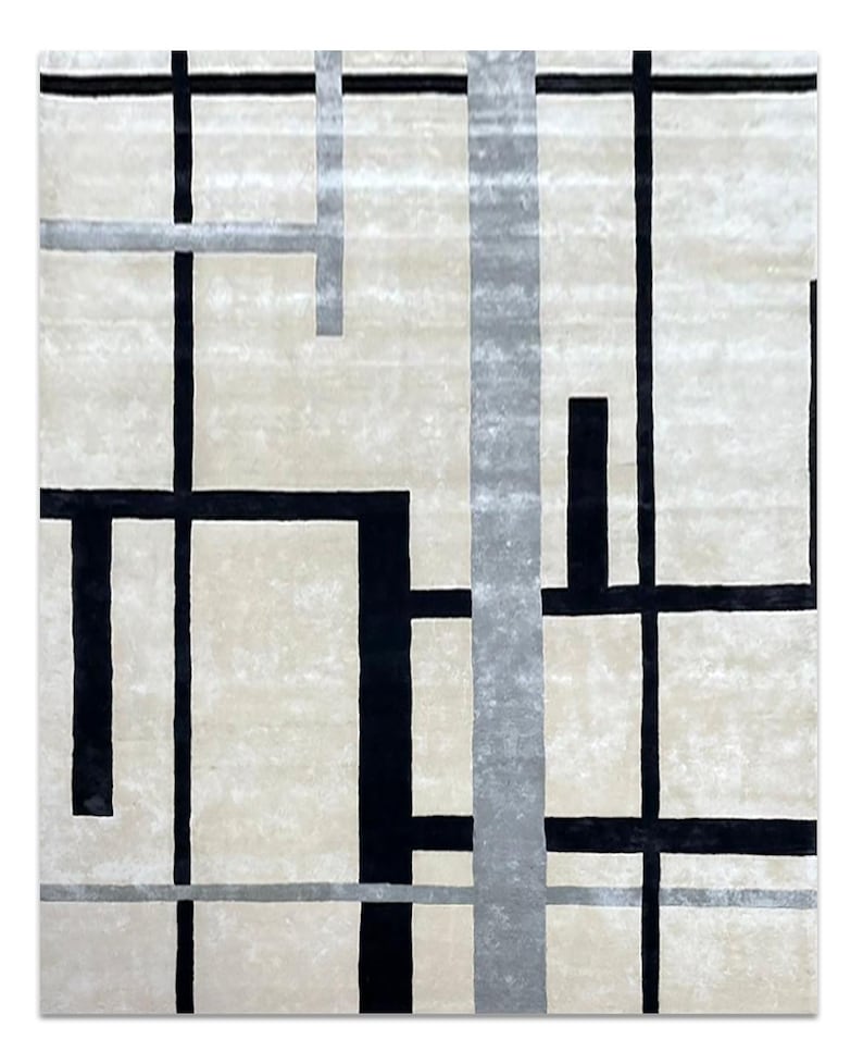 May include: A square rug with a cream-colored background and a geometric design. The design features black and gray lines of varying widths, creating a modern, abstract pattern. The rug's texture appears soft and plush.