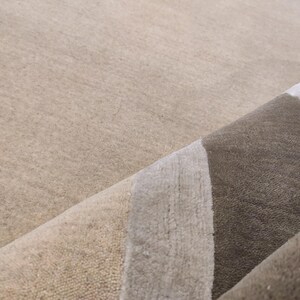May include: Close-up of a rolled-up area rug with a neutral color palette. The rug features a beige background with a design of vertical stripes in shades of gray and brown. The texture of the rug is visible.