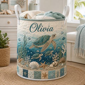 May include: A cylindrical quilted laundry hamper featuring a sea turtle print in shades of blue and teal, with the name Olivia embroidered in dark blue script. The hamper has two white fabric handles and a base border with starfish and coral.